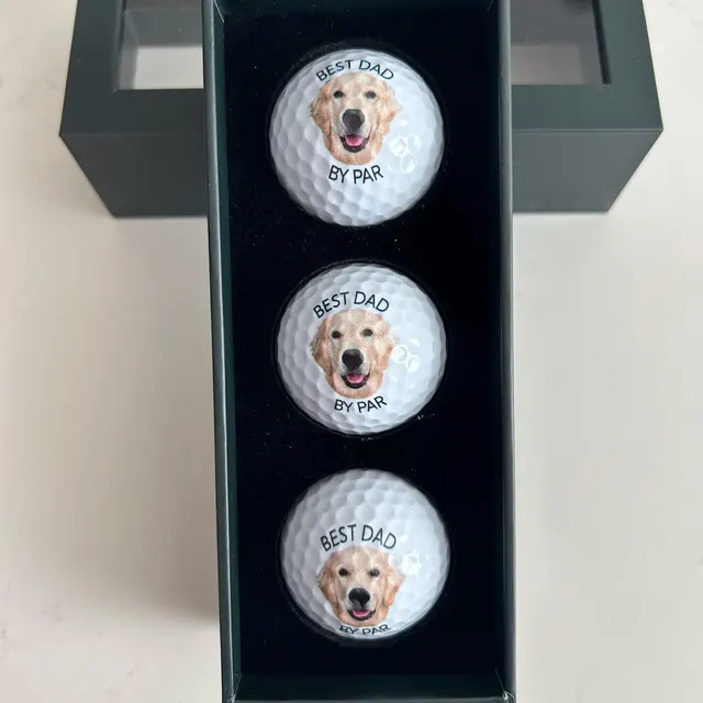 Three golf balls printed with a golden retriever, in the gift box
